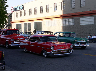 [A red two-door car in front of a red pickup truck and beside a green car.]